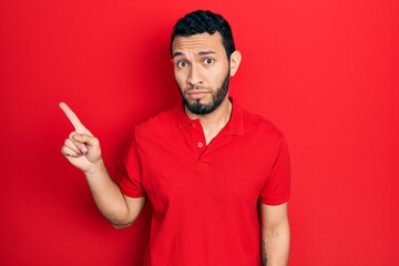 Hispanic man with beard pointing with fingers to the side clueless and confused expression. doubt concept.