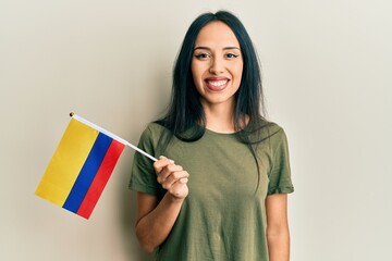 Young hispanic girl holding colombia flag looking positive and happy standing and smiling with a confident smile showing teeth
