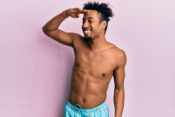 Fototapeta premium Young african american man with beard wearing swimsuit very happy and smiling looking far away with hand over head. searching concept.