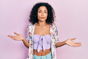 Young latin girl wearing casual clothes clueless and confused expression with arms and hands raised. doubt concept.