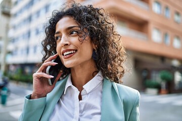 Young hispanic business woman wearing professional look smiling confident at the city speaking on...