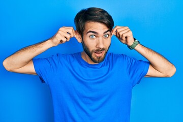 Young hispanic man wearing casual clothes smiling pulling ears with fingers, funny gesture....