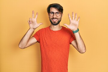 Naklejka premium Young hispanic man wearing casual clothes and glasses showing and pointing up with fingers number eight while smiling confident and happy.
