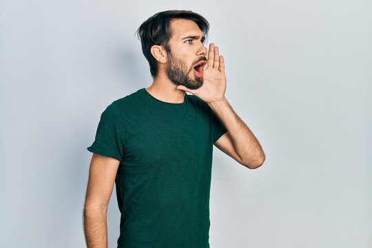 Young hispanic man wearing casual white tshirt shouting and screaming loud to side with hand on mouth. communication concept.
