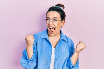 Young hispanic woman wearing casual clothes and glasses screaming proud, celebrating victory and...