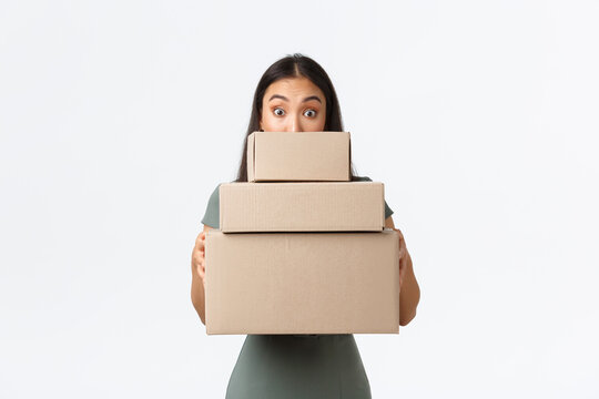 Small Business Owners, Startup And Work From Home Concept. Cute Asian Girl Looking Behind Pile Of Boxes With Purchsed Items From Online Shops, Collect Delivery From Post-office, White Background