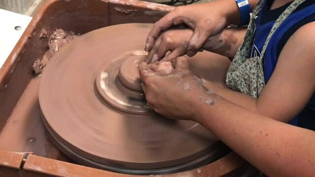 Hands of mother and child shaping clay on a ceramics pottery wheel