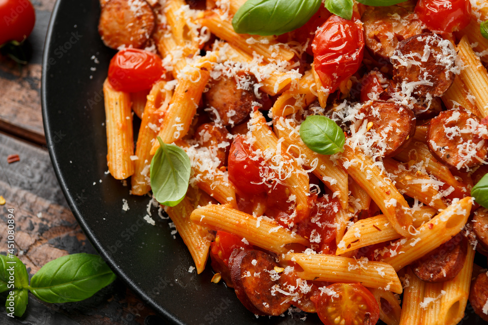 Wall mural Sausage penne Pasta with tomato sauce, parmesan cheese and basil on black plate