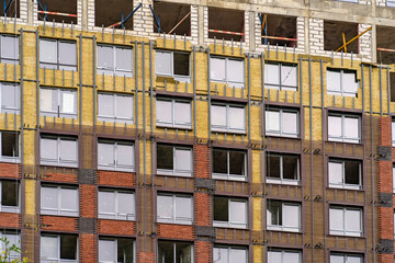 Fototapeta na wymiar Monolithic concrete frame of apartment building under construction with partially attached ready-made facade cladding blocks. Exterior passive house wall heat insulation with mineral wool.