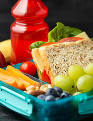Healthy school, work lunch box with sandwiches and fresh vegetables, nuts, bottle of juicy and fruits on wooden table