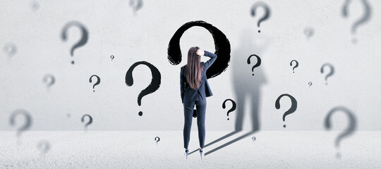 Solution and doubt concept. Attractive young european businesswoman standing in concrete interior with question marks sketch and shadows.