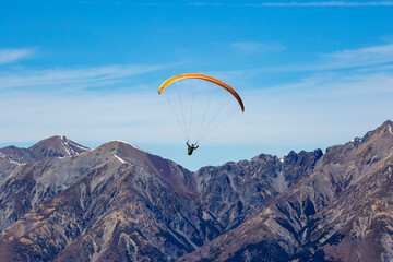 A paraglider takes off from Mt Cheeseman and flies through the Craigieburn Valley towards the Torlesse Range in New Zealand