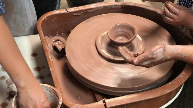 Hands of mother and child shaping clay on a ceramics pottery wheel