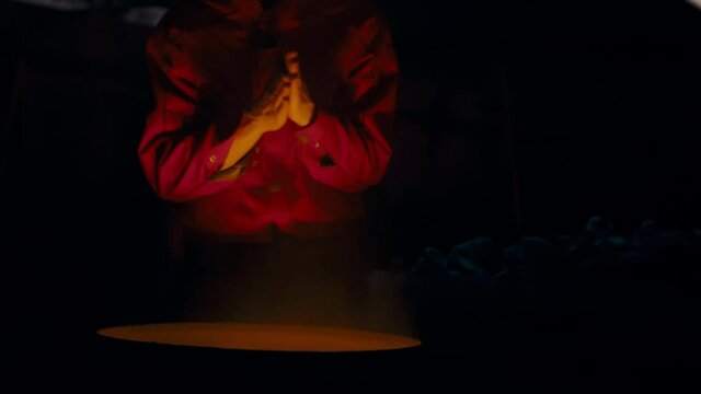 A European man in glasses and a red jacket basking near a burning garbage can on his face.