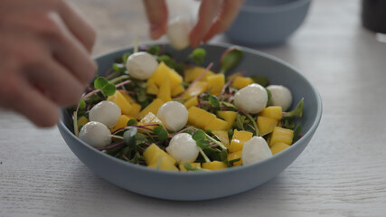 Man put mozzarella balls in salad with micro greens in blue bowl