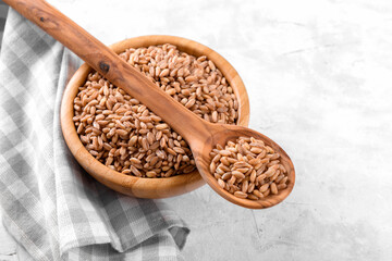 Wholegrain uncooked raw spelt farro in wooden spoon and bowl on grey stone table background, food cereal background, close up, top view