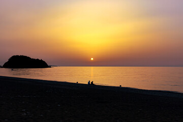 Silhouette of two men fishing by the seaside at dawn. Sun rises over the Mediterranean Sea in Cirali, Antalya, Turkey. Selective focus.