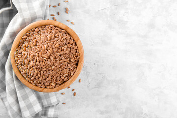 Wholegrain uncooked raw spelt farro in ceramic bowl with napkin on grey stone table background, food cereal background, view from above, copy space