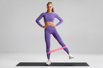Fitness woman doing exercise for glutes with resistance band on gray background. Athletic girl working out