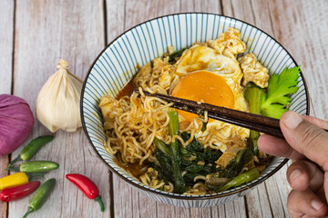 A serving of instant noodle with chicken, sunny side up and veggies. Selective focus points. Blurred background