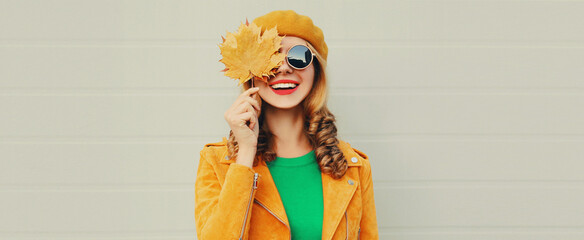 Autumn portrait of beautiful happy smiling young woman with yellow maple leaves wearing a french beret on gray background
