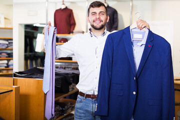 Obraz premium smiling young owner guy displaying jacket in fashion store
