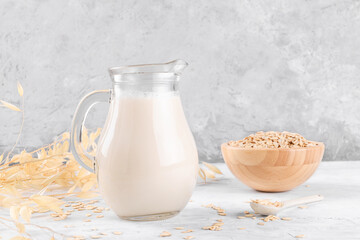 Vegan non dairy alternative milk. Oat milk in a jug on a grey stone table background and a bowl with oat flake copy space