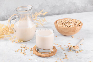 Vegan non dairy alternative milk. Oat milk in a jug on a grey stone table background and a bowl with oat flake on grey stone table