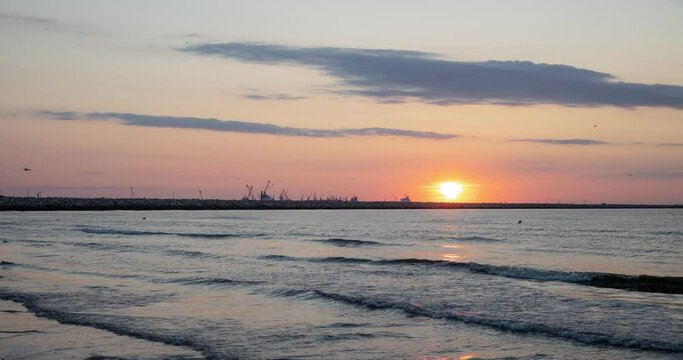 Landscape with sunrise on the Black Sea beach. The timelapse captures a boat with fishermen returning from the sea, and a lot of seagulls flying in search of fish and shells.
