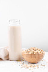 Vegan non dairy alternative milk. Oat milk in a bottle and a bowl with oat flake on white table background, copy space