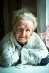 Portrait of an old lady in her house near the window.