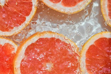 Close-up fresh slices of red grapefruit on white background. Slices of grapefruit in sparkling...