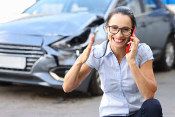 Satisfied woman talking on mobile phone near wrecked car