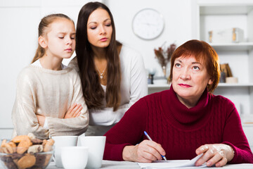 Dissatisfied woman with daughter gazing at her mother writing letter at home