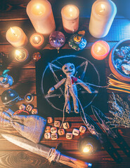 Voodoo doll studded with needles in center of magical table with candles and occult objects top view. Magic and dark spooky ritual. Retribution or revenge through witchcraft concept.