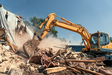 Destruction of old house by excavator with lot of dust. Bucket of excavator breaks concrete structure.