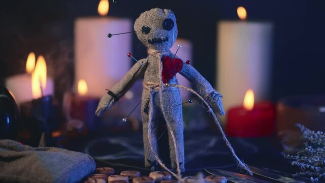 Voodoo doll studded with needles in magical table with candles and occult objects. Magic and dark spooky ritual. Retribution or revenge through witchcraft concept.
