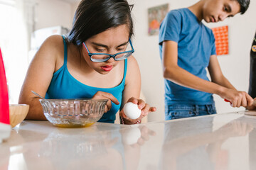 Latin teenager girl with down syndrome and her brother cooking at home, in disability concept in...