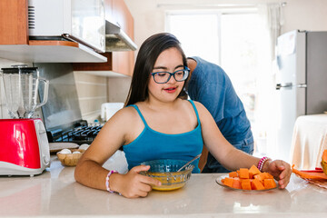 Latin teen girl with down syndrome eating fruit in the kitchen, in disability concept in Latin...