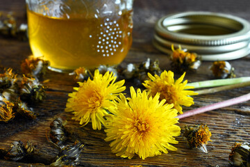 A close up image of a jar of home made dandelion syrup with both fresh and dried dandelions on a...