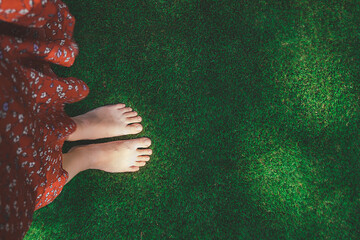 women bare feet on flat green grass lawn, top view. woman dressed in red dress. walking with bare feet on natural textures. selective focus