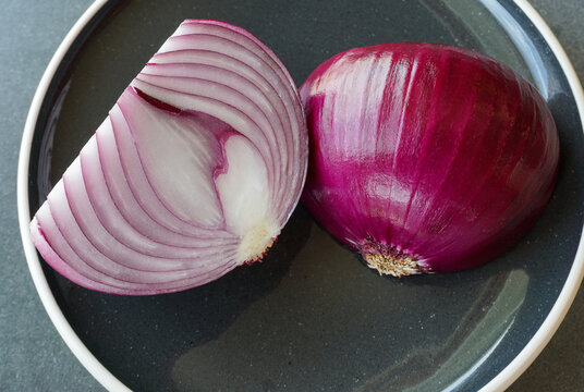 Sliced red onion halves on a black plate, accentuating the spicy ingredient's rich purple color, inner pattern.