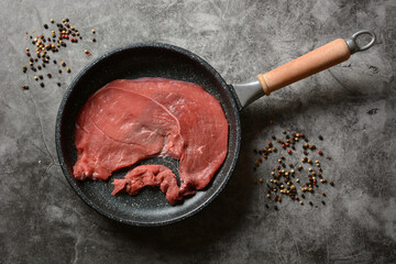 raw veal slice in pan - gray background - horizontal - closeup