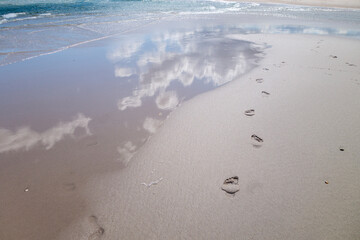 bare foot prints on we sand coastal beach with waves and sky reflections