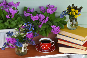 Still life with primula and pansy viola flowers, cup of tea and pile of poem books outside in porch.