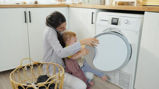 Caucasian busy mother doing housework with baby boy toddler in kitchen