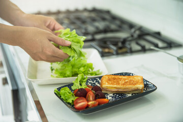 Woman cooking sandwich with salad in the rustic kitchen. Woman preparing tasty bruschettas in kitchen. Woman making tasty sandwich with salad on table.