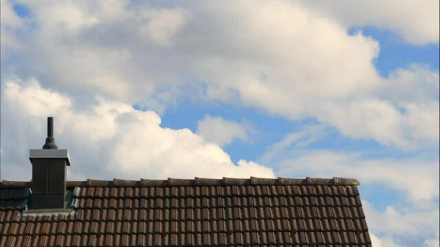 Time lapse shot of flying white clouds on blue sky behind rooftop of house 