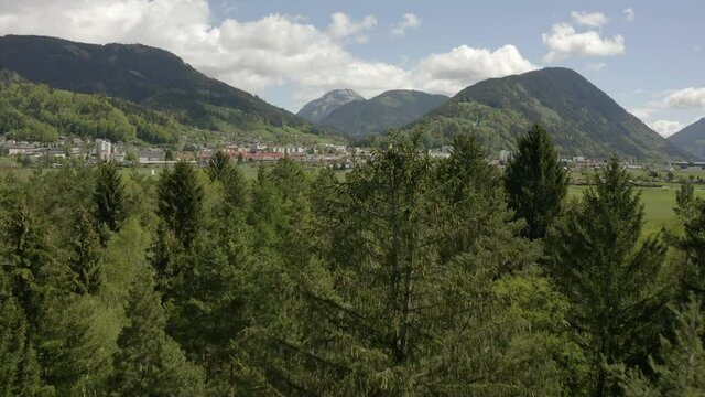 Aerial view moving forward shot, Passing pine trees and revealing scenic view of the city of Liezen in Austria.