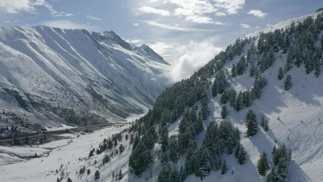 Aerial view moving forward shot, Scenic view of snow covered mountains in K&uuml;htai Glacier in Tyrol, Austria, Sun light and Cloudy Sky in the background.